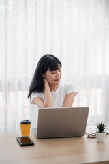 Young Woman Working on Laptop at Home Office with Coffee and Smartphone on Desk, Bright Natural Light Through Sheer Curtains, Casual and Relaxed Work Environment