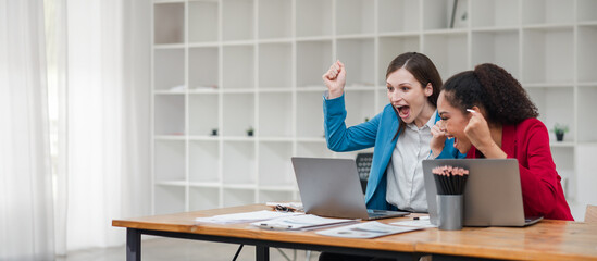 Obraz premium Two Excited Businesswomen Celebrating Success at Work in Modern Office with Laptops and Documents on Desk
