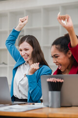 Two Excited Businesswomen Celebrating Success at Work with Laptops in Modern Office Environment
