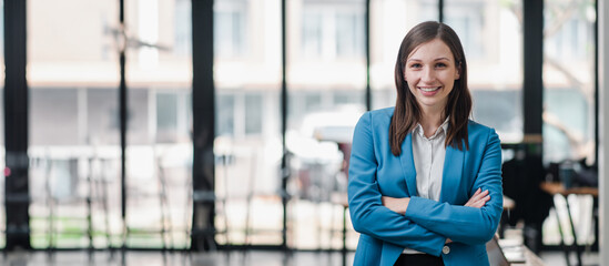 Confident Businesswoman in Blue Blazer Standing with Arms Crossed in Modern Office Environment with...