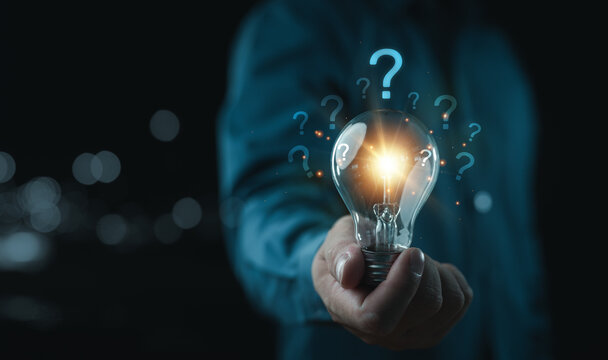 Businessman holding glowing lightbulb and question mark with copy space for creative thinking idea and problem solving concept.