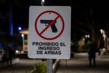Sign with crossed hand gun and sign in Spanish entry with weapons prohibited at a central park in a small tourist town. Concepcion de Ataco, El Salvador.
