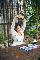 Woman streching arm raised sitting incorrect position home office desk. Back side of young asian...