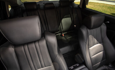 Close-up  leather  black     rear seat made of  in the background passenger seats with seat belts. Luxury car interior