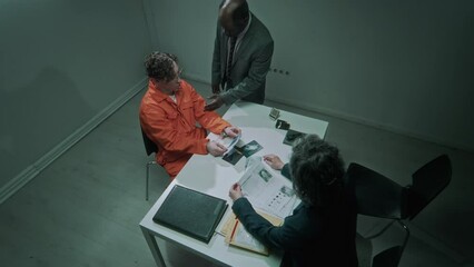 Full top shot of diverse federal agents interrogating murder suspect, looking at crime scene photos, African American officer grabbing defendant by throat for intimidation, female partner stopping him
