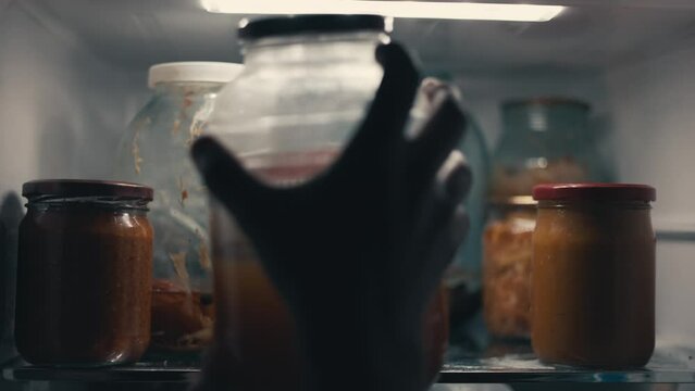 man opens the refrigerator at night and takes out a glass jar of kvass