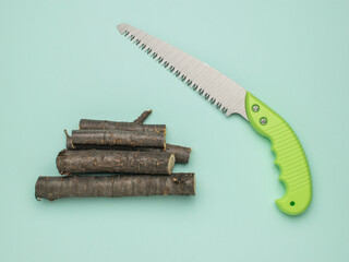Hand Saw with Stack of Wood Logs on Turquoise Background - DIY, Carpentry, and Gardening Tools © kvladimirv