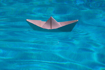 Paper ship sail. Paper boat on the sea water background. Dreaming traveling. Blue water background.