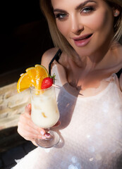 Cocktail party concept. Sensual woman wearing a white cocktail dress drinking a tropical cocktail....