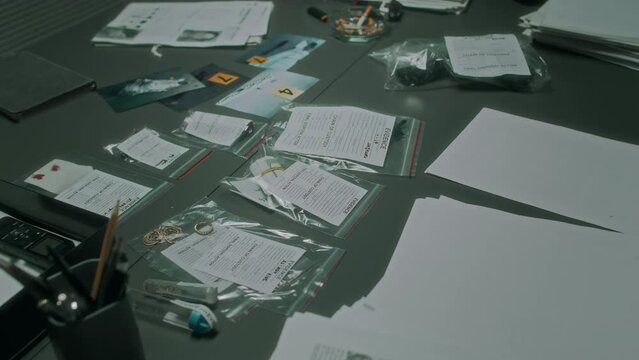 Close-up no people shot of forensic evidence objects in plastic bags, laid out on table at police department, case files, documents, criminal profiles, during investigative work