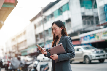 Fototapeta premium Portrait of a smiling busy business woman leader wearing suit standing. businesswoman leader wearing suit thinking of success, Smiling woman holding smartphone walking on street outdoors.