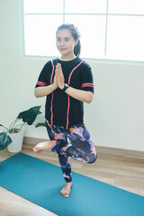 Sporty woman stand on one leg keeping balance, yoga and meditation time at home.