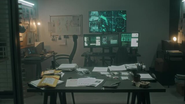 Full dolly-in no people shot of screen with satellite surveillance footage, computer screens with suspect photo and fingerprints, crime maps, table with evidence in envelopes, at police station