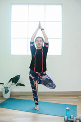 Sporty woman stand on one leg keeping balance, yoga and meditation time at home.
