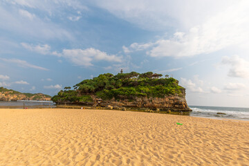 Scenic Coastal View with Lush Green Island and Golden Sandy Beach Under a Blue Sky with Clouds ; indonesia tourism drini beach