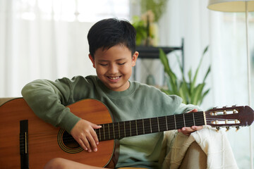 Smiling boy enjoying playing guitar at home