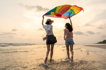 Young couple asian lesbian with pride movement LGBT holding rainbow flag for freedom. Demonstrate...