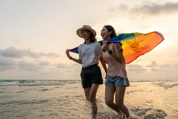 Young couple asian lesbian with pride movement LGBT holding rainbow flag for freedom. Demonstrate...