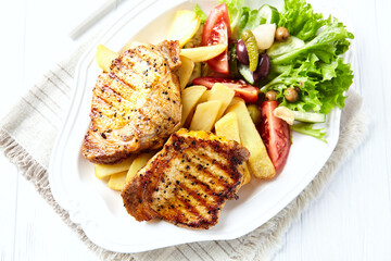 Grilled Steaks with french fries and fresh salad. Bright wooden background. Top view.