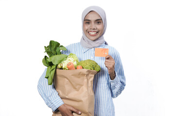 Young woman wear casual clothes hold brown paper bag with vegetable products mock up of credit bank card isolated on white background studio portrait