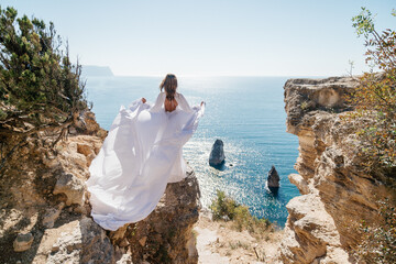 A woman in a white dress is standing on a rocky beach with her hat on. The scene is serene and peaceful, with the woman enjoying the view of the water