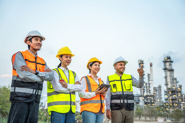 Group of Asian engineer people with safety helmet standing front of oil refinery. Industry zone gas...