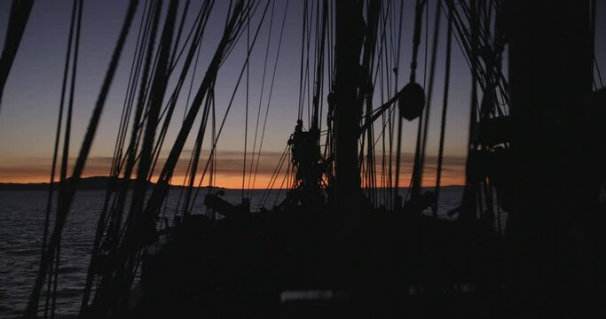 1700s sailing ship underway at sunset. Heavy seas. Static wide shot of bow in silhouette.