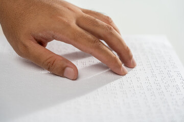 Hand of a blind person reading some braille text on page paper to learn. Finger of blind student touching the braille alphabet Code on sheet.