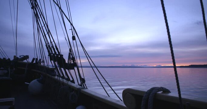 1700s sailing ship underway at sunrise. Steady wide shot of the starboard bow, anchor, and lines. Wide shot.
