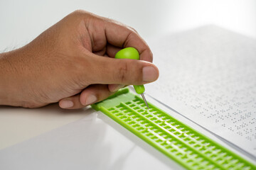 Close up Hand of a blind person writing some braille text on page paper. Young blind man using...