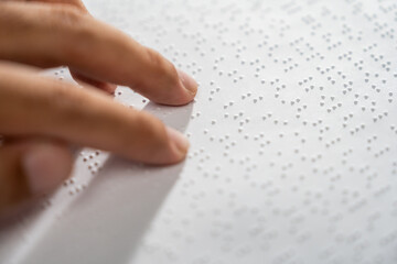 Hand of a blind person reading some braille text on page paper to learn. Finger of blind student...