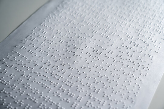 Close up some braille text on page paper written by blind. Blind man using slate and stylus tools making embossed printing the braille alphabet Code on sheet.