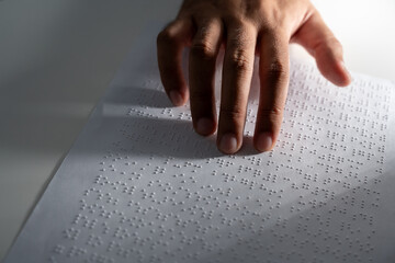Hand of a blind person reading some braille text on page paper to learn. Finger of blind student...