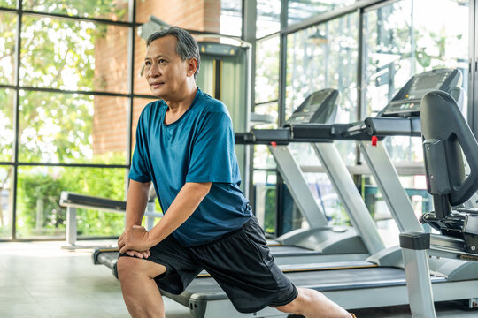 Senior asian man wearing sportswear warming up in fitness gym before exercise. Mature man stretching arm before running. Training athlete work out