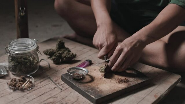 The hands of a junkie are cutting marijuana to prepare for consumption.