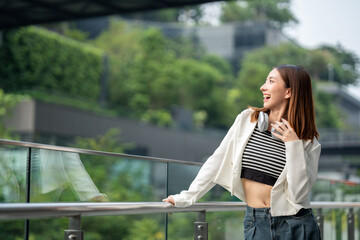 Young asian woman fashion lifestyle with headphone standing posing in urban city downtown. Happy...