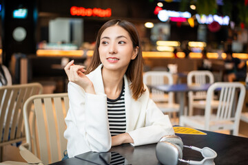 Young asian smiling woman sitting in the coffee shop cafe. Happy Business woman with white suit laughing talking with friend inside restaurant. People lifestyle concept.