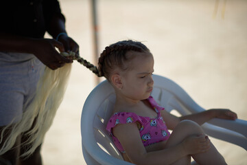 holding braids with pink color on little kid head. stylist applying braiding hair on young baby.