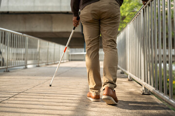 Young blind man walking in city with walking stick. Visually impaired man difficult to traveling on...