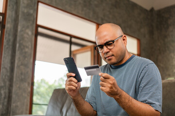 Asian handsome man holding credit card can't input number in smartphone for payment online feeling...