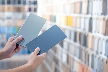 Designer hands compare two gray laminate sheets nearby material swatch wall display in material...