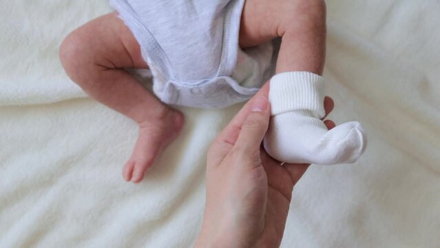 Close up of caring unrecognizable mother putting tiny socks on baby's feet baby wearing bodysuit lying on bed