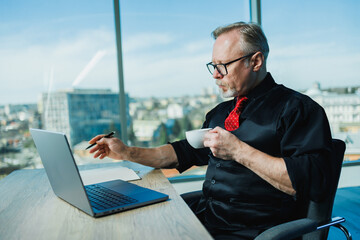 Male gray-haired stylish freelancer working with laptop, gray-haired businessman at workplace in...