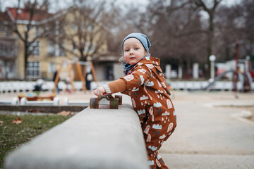 Cute toddler girl playing outdoor in playground with skateboard. Girl in softshell bodysuit...