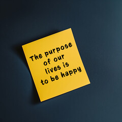 A yellow sticky note with the handwritten inspirational quote "The purpose of our lives is to be happy" placed on a dark background, conveying a positive message