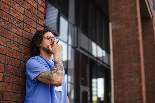 Healthcare worker taking a break, smoking a cigarette outdoors, in front of the hospital building.
