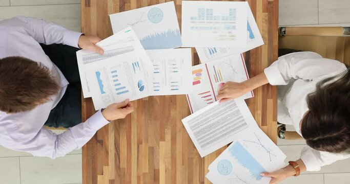 Two colleagues analyze financial reports and discuss the company future strategies in office top view