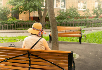 old lonely woman with hat sitting on bench with park 