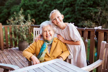 Portrait of granddaughter spending time with elderly grandma, companionship. Senior lady sitting on patio.