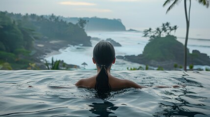  A woman sits in a pool facing the ocean, with a cliff as her backdrop Palm trees line the shoreline, and the foreground features a body of water